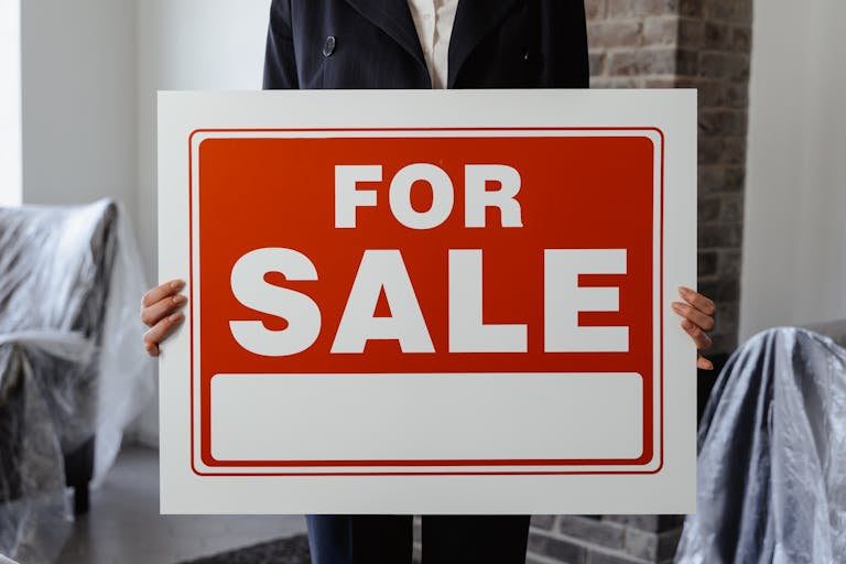 FHA Down Payment Assistance. Close-up of a person in a suit holding a For Sale sign in a furnished room.