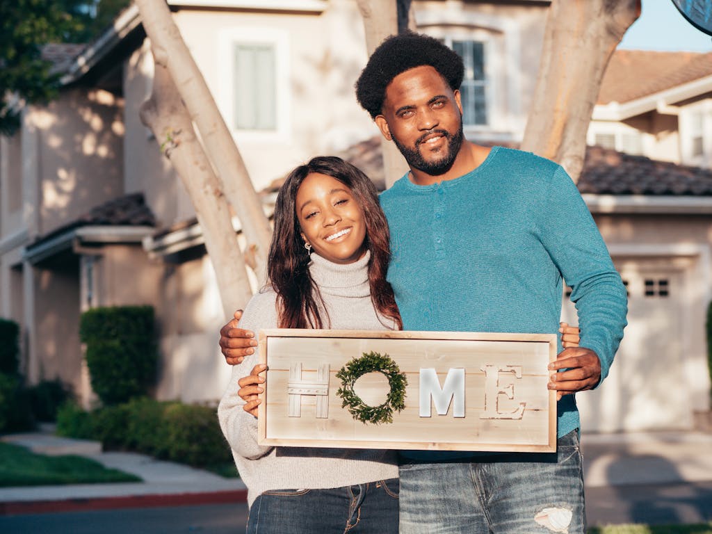 Florida Hometown Heroes helps a happy couple holding a 'Home' sign in front of their new house, symbolizing joy and togetherness.