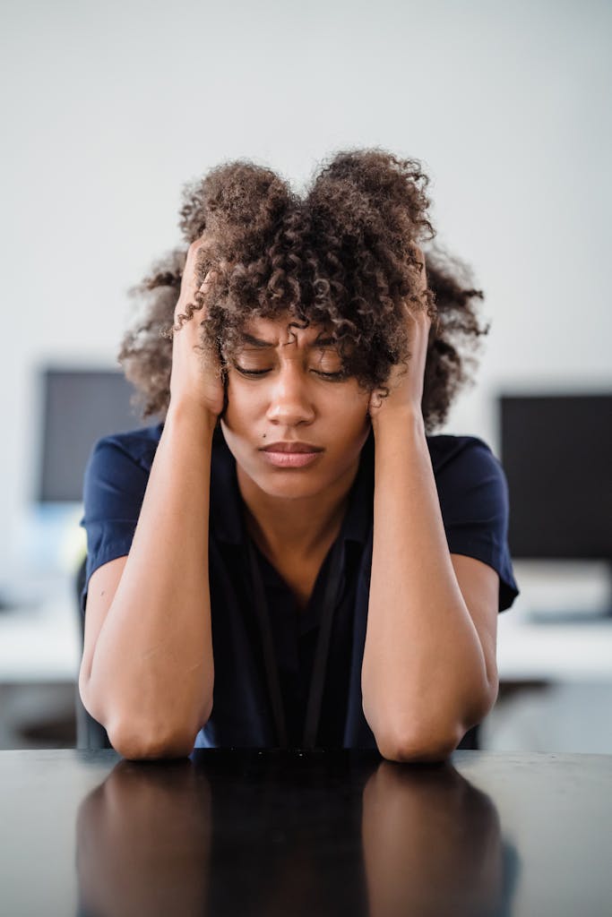 Woman in office setting expresses stress, seated at desk with hands in hair thinking about the subscription to struggle. 
