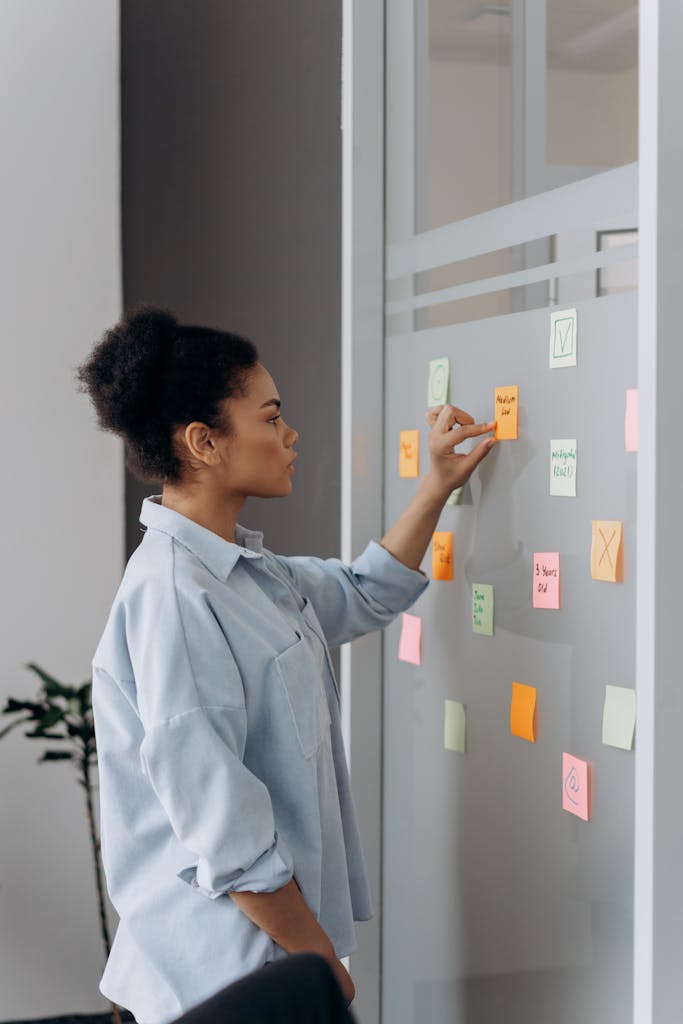Young professional organizing tasks on a glass board with colorful sticky notes in an office setting trying to escape the subscription to struggle.